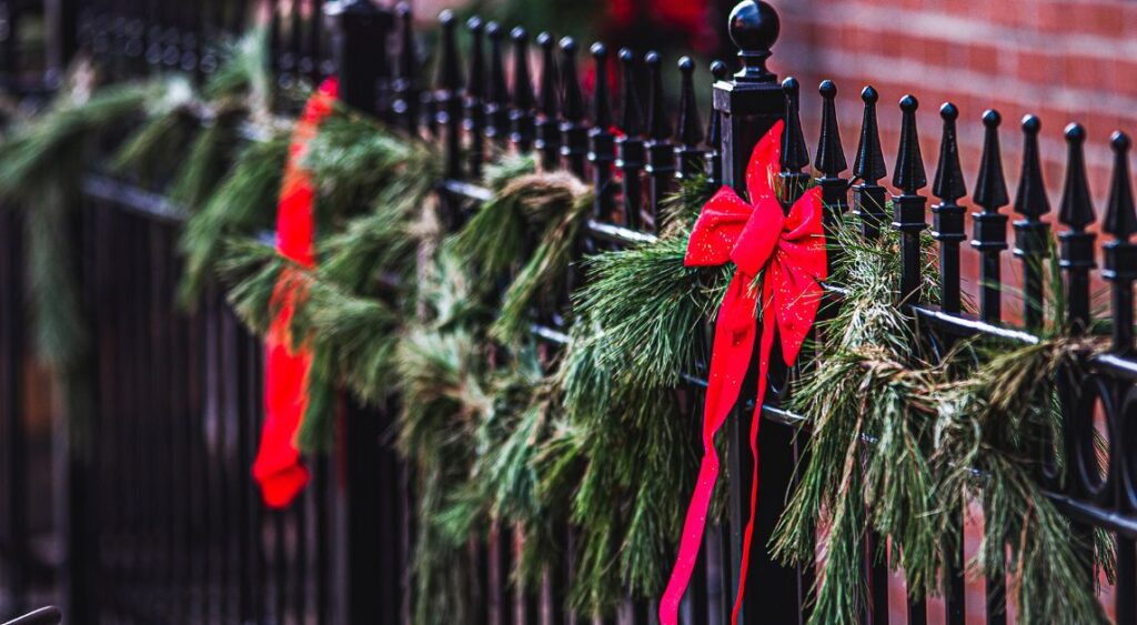 A Wrought Iron Fence Decorated With A Garland For The Holidays